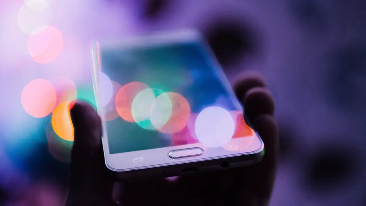 Hand holding a smartphone against colorful city lights at night