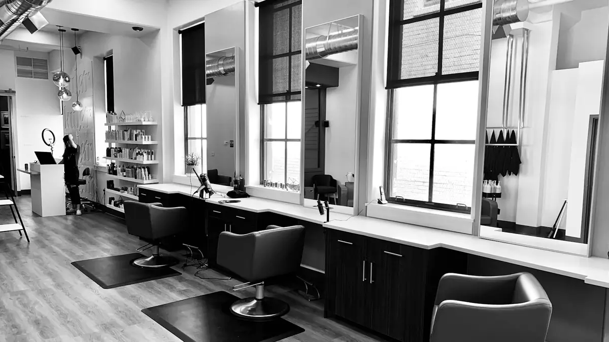 Black-and-white photo of a modern salon with styling chairs and large windows