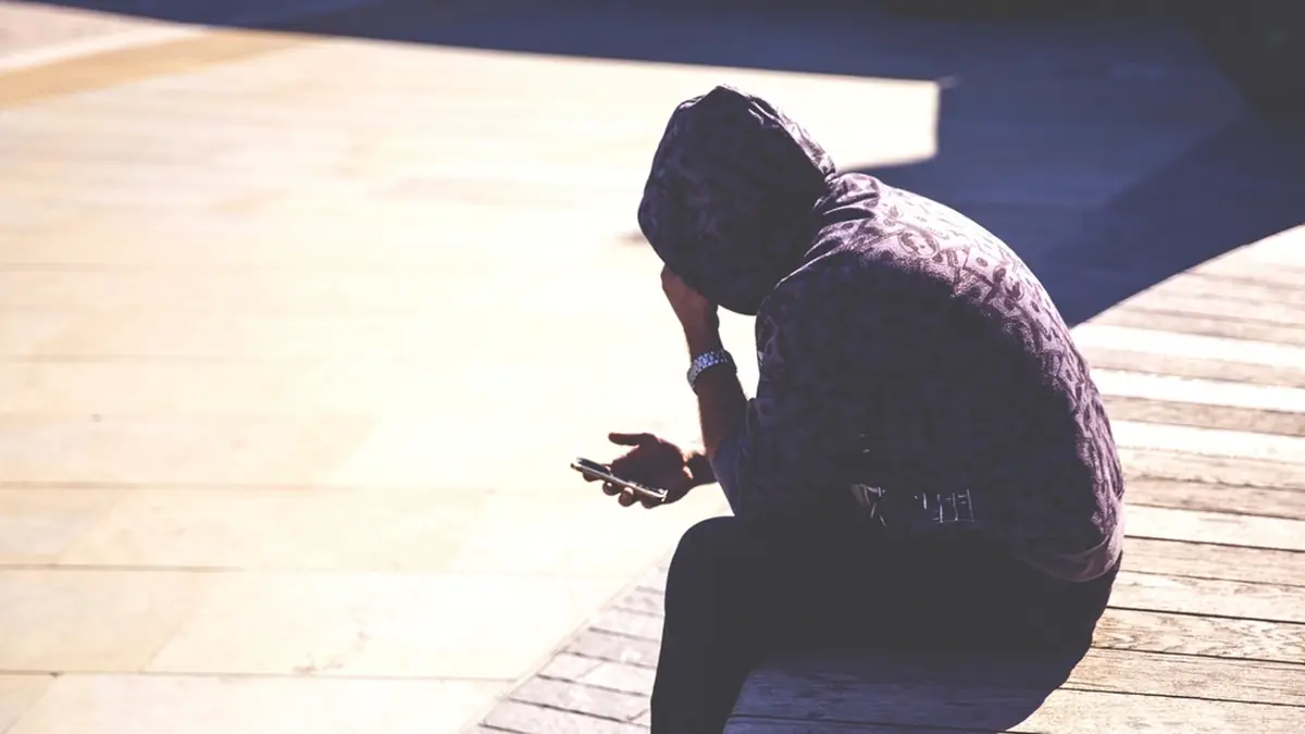 Person in a hoodie checking a smartphone in dim light
